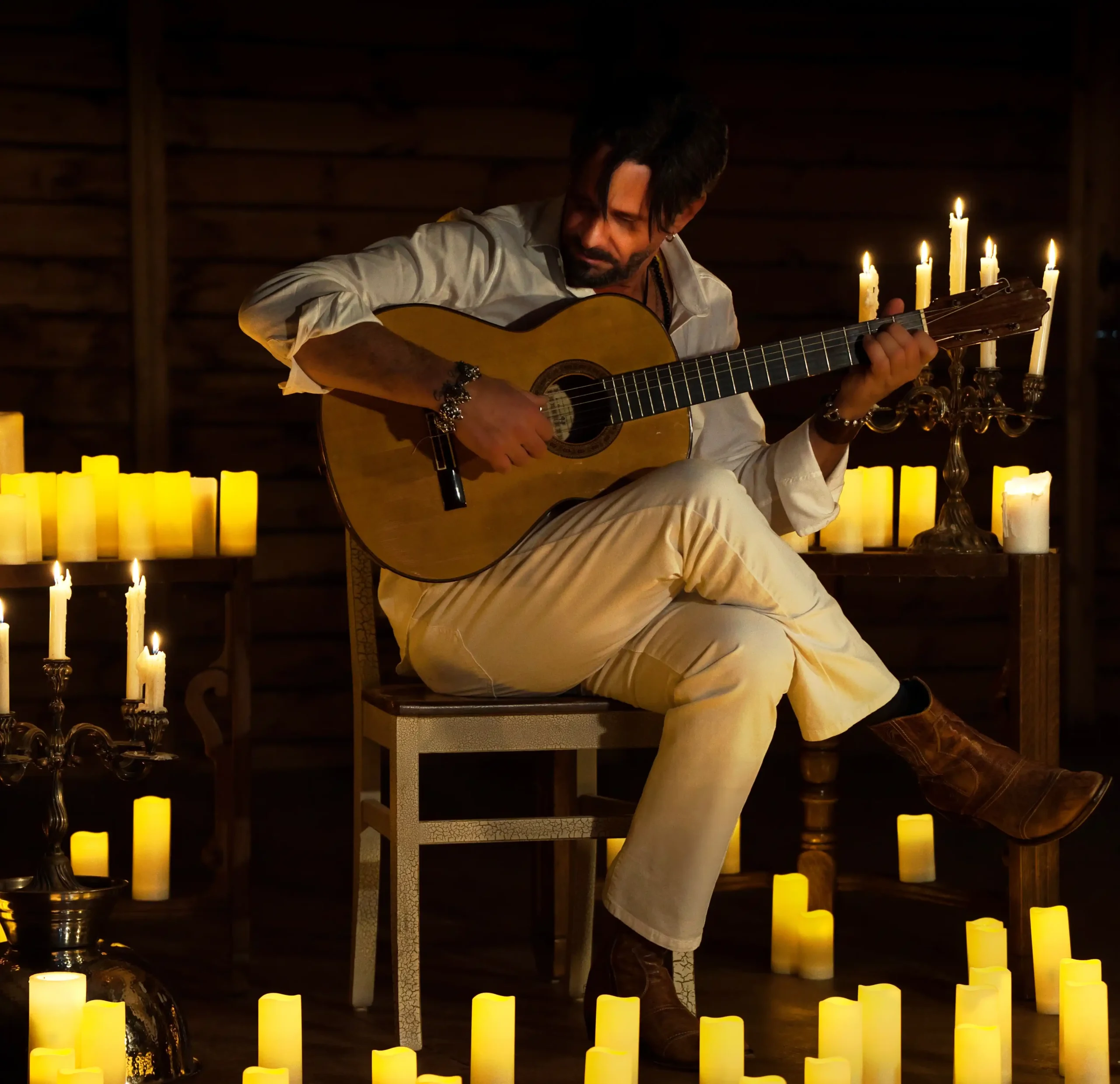 Emilio playing guitar surrounded by glowing candles in a cozy, dimly lit room.