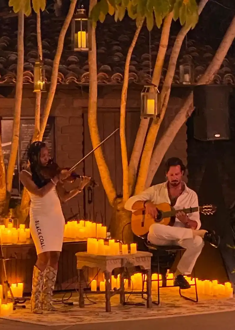 Emilio performing alongside a violinist under soft lantern lights surrounded by candles.