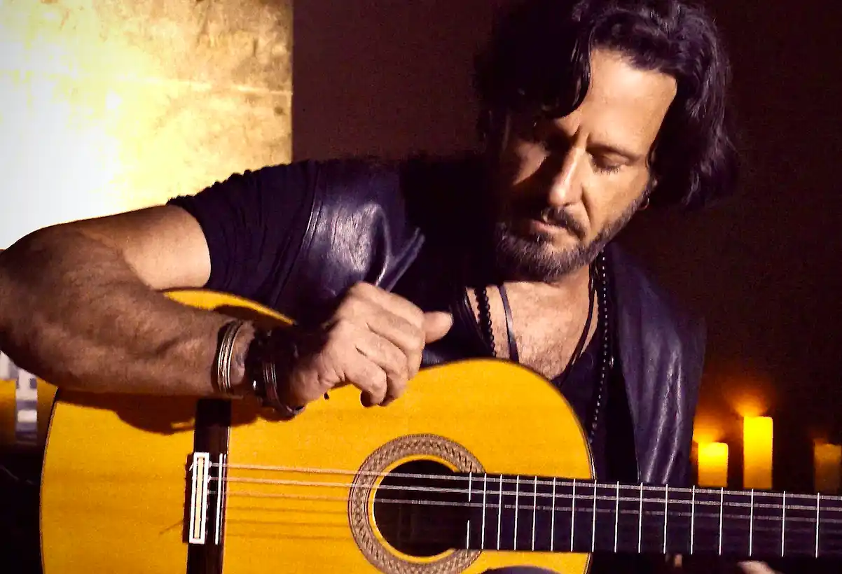 A close-up of Emilio intensely focused while playing his guitar in a dimly lit setting.