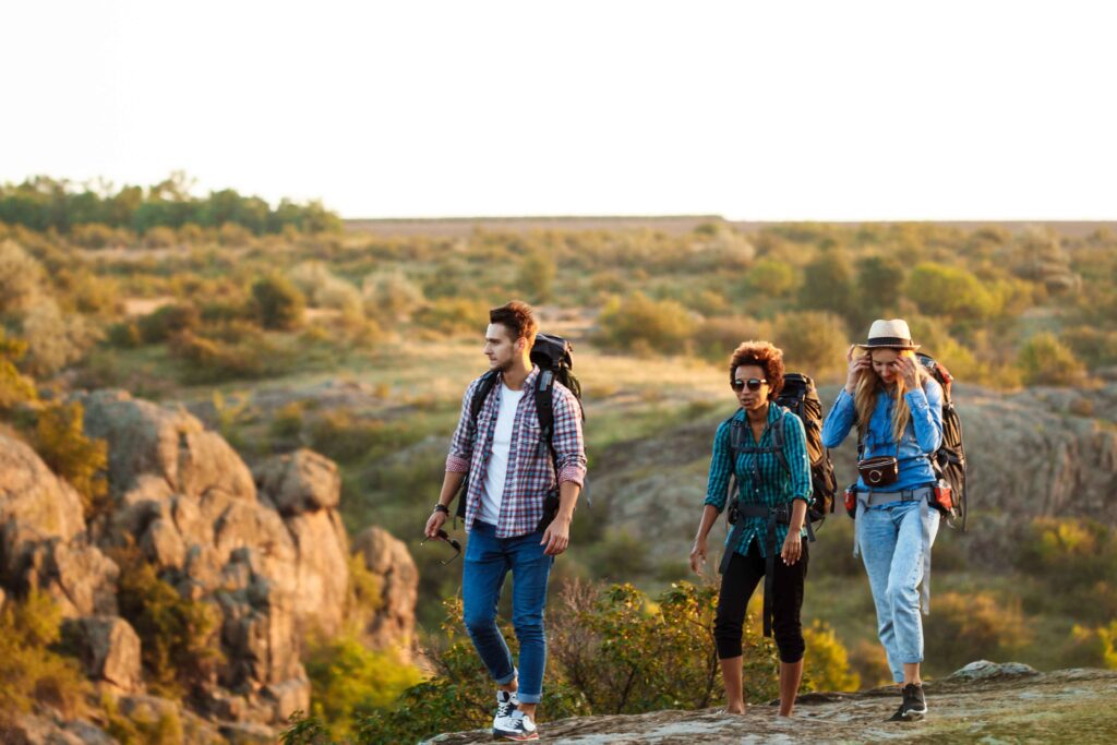 Group of young, cheerful travelers with backpacks smiling and walking through a scenic setting during an outdoor adventure.
