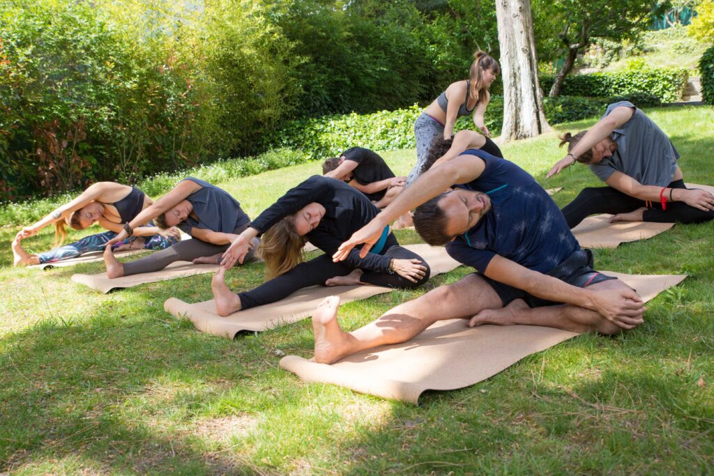  Group of people practicing yoga together, stretching their bodies in a serene indoor space, suggesting a peaceful and focused yoga retreat environment.